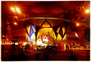 Photograph by Richard Heeps. Photograph taken at night of the front of a brightly lit hotel. The scene is bathed in golden and reddish brown colours. The name of the hotel is La Concha and its name is written in white neon against a red and golden shell design. The photograph is taken through glass and there are reflections of cars as well as the room from which the photograph is taken.