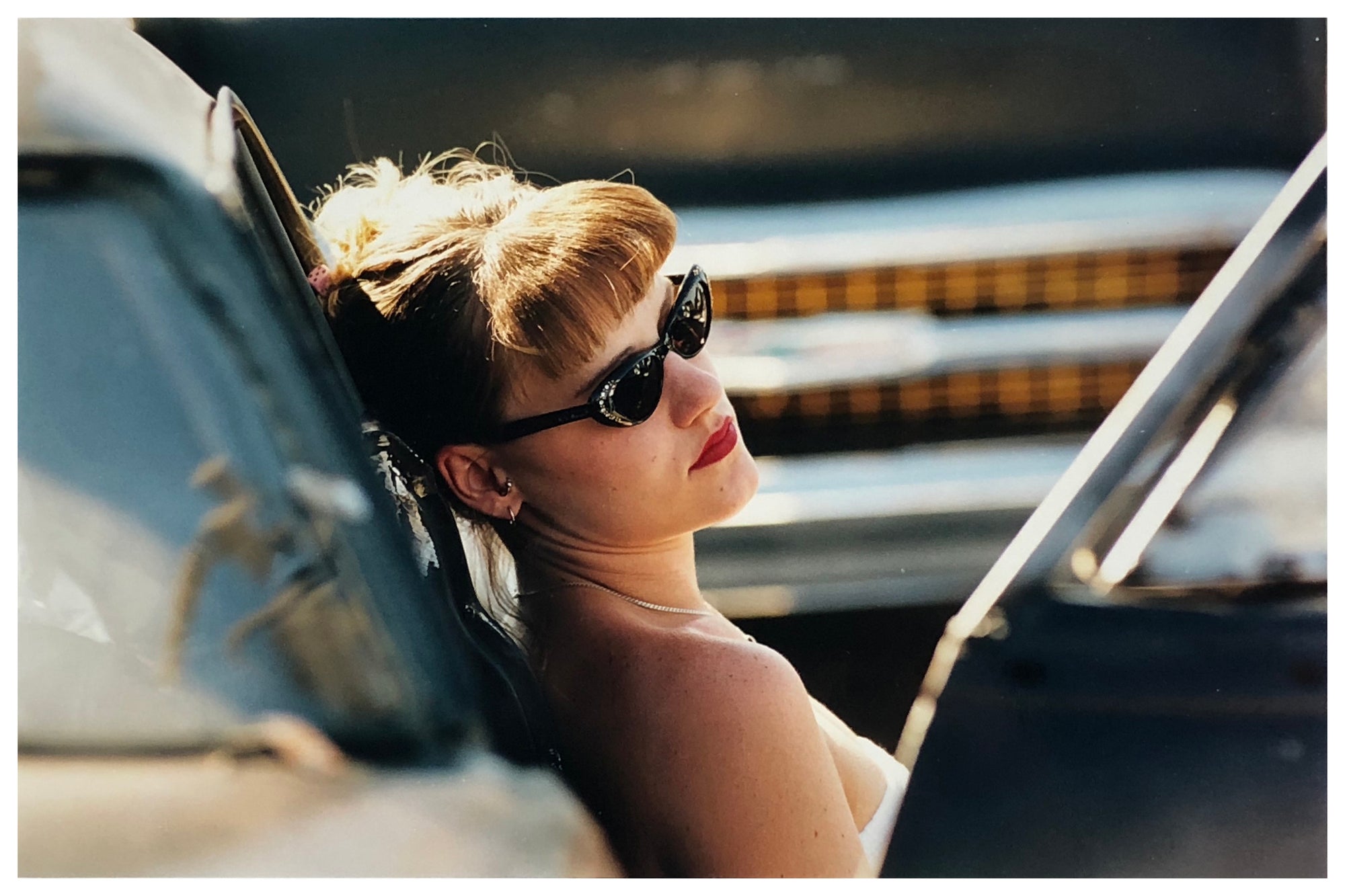 Photograph by Richard Heeps.  A woman rests on the side of a car.