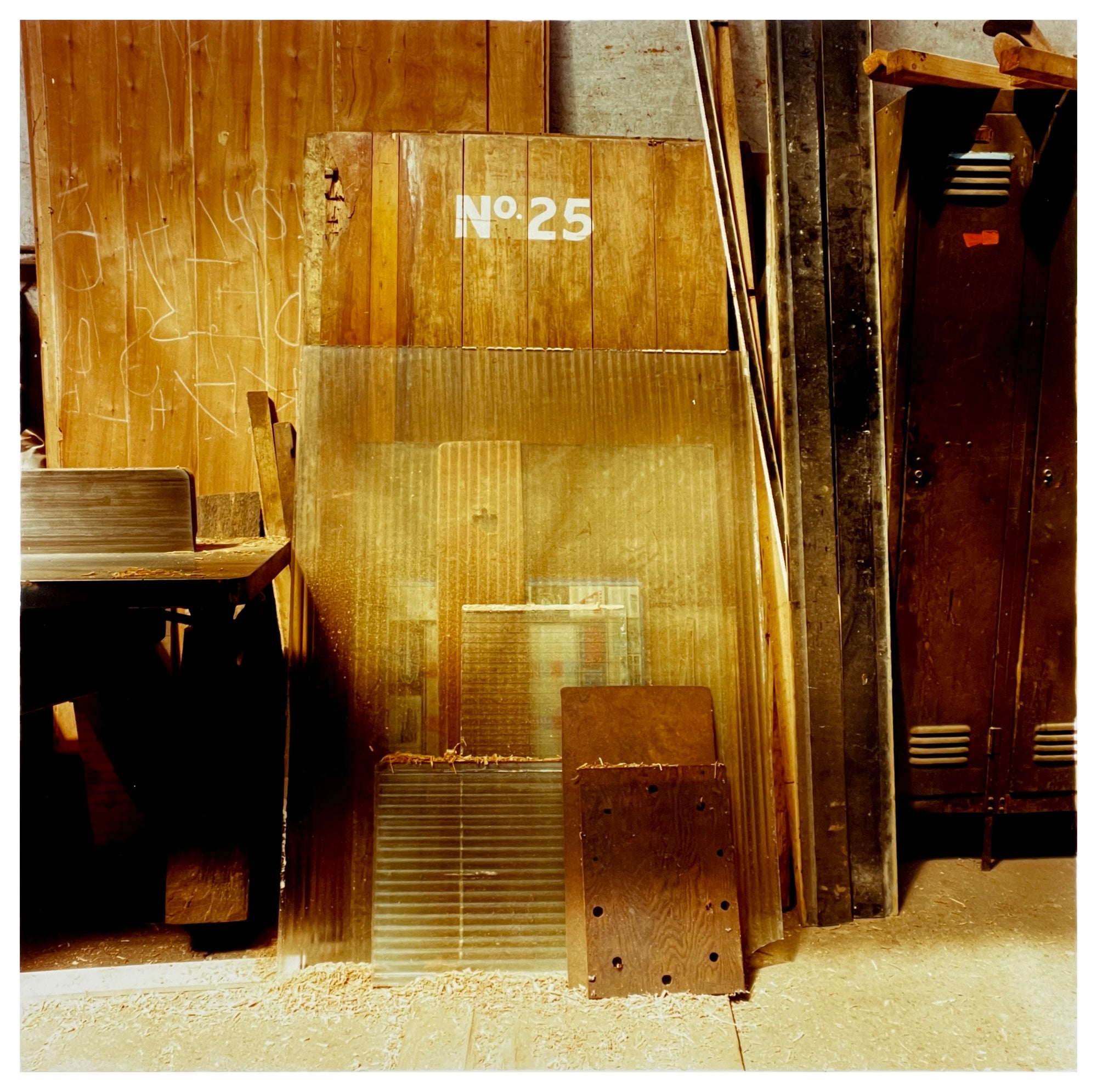 Photograph by Richard Heeps.  Inside the workshop old doors, bits of wood and corrugated plastic are leaning against the wall.  An old door has No.25 printed on it.