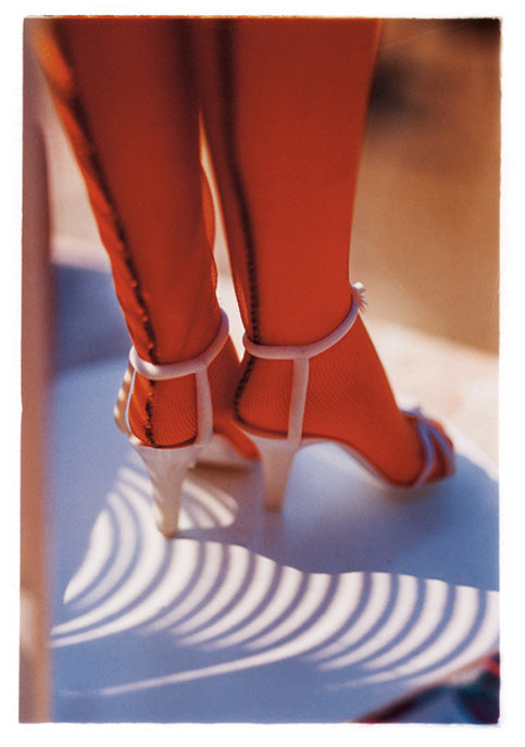 Photograph of a ladies calves, feet in strappy heels and seemed nude nylon tights. A shadow cast across the floor.