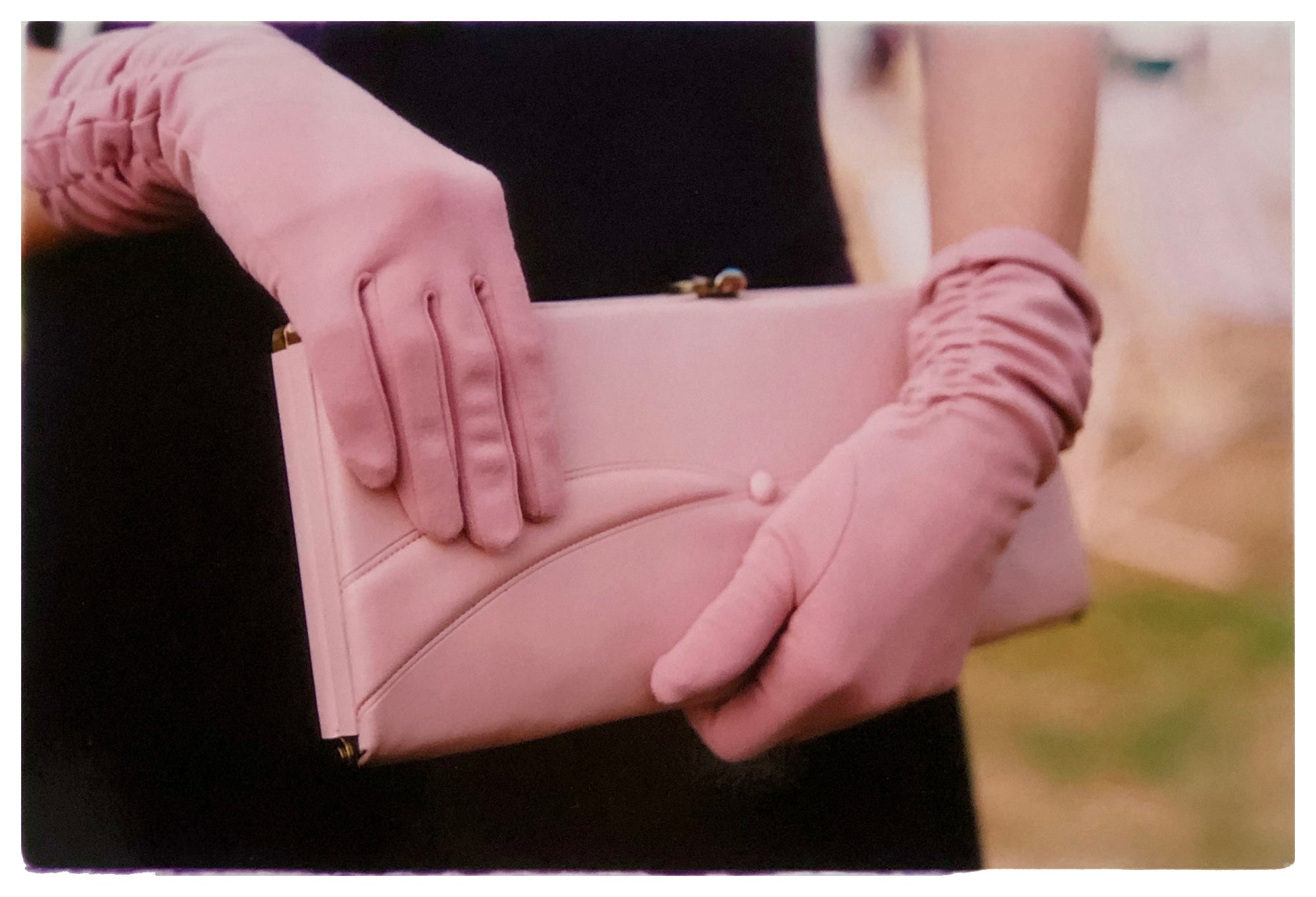 Photograph by Richard Heeps.  Pink clutch bag being held by matching pink gloved hands, set against the wearer's black dress.