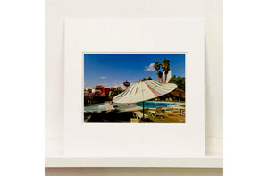 A vintage parasol, poolside at the El Morocco Motel, Las Vegas, Nevada, overlooked by palm trees, blue skies and iconic neon signs. Part of Richard Heeps' 'Dream in Colour' series.