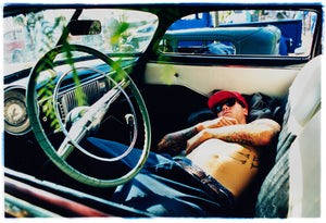 Photograph by Richard Heeps. Inside a classic American car and lying on the seats is a man resting.