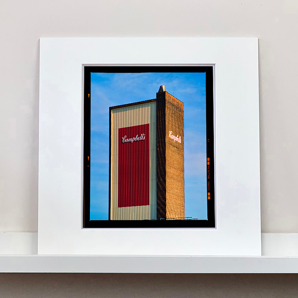 Photograph by Richard Heeps.  The Campbell's factory tower, cream and red with the Campbell's logo in the middle, against a blue sky.