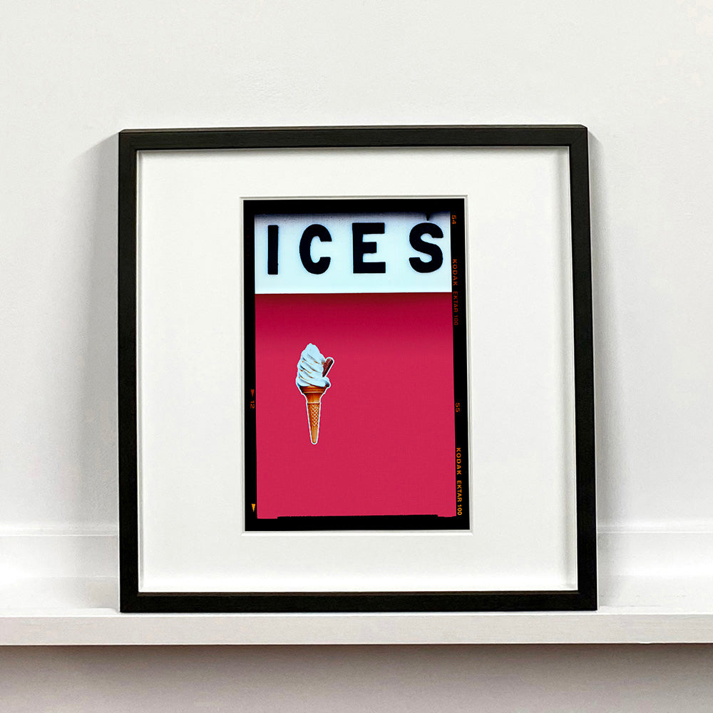 Black framed photograph by Richard Heeps.  At the top black letters spell out ICES and below is depicted a 99 icecream cone sitting left of centre against a raspberry coloured background.  