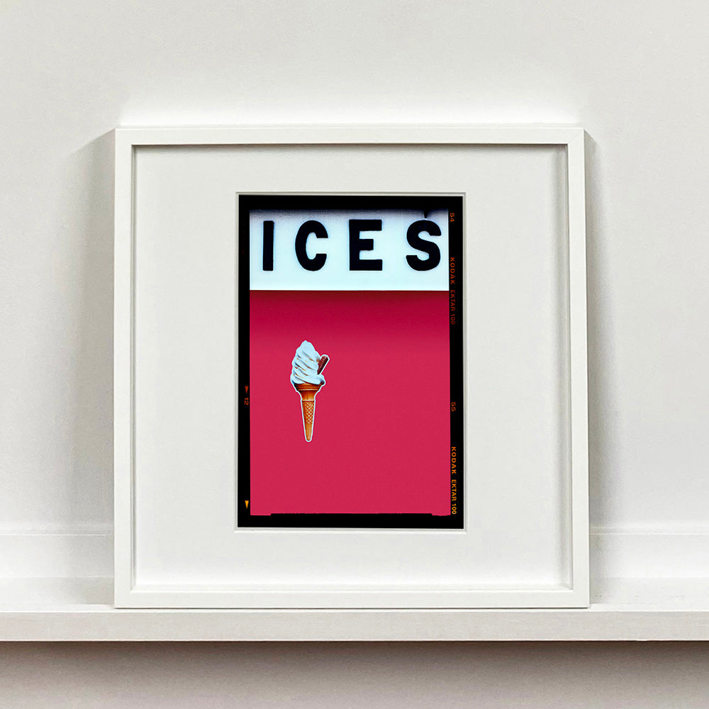 White framed photograph by Richard Heeps.  At the top black letters spell out ICES and below is depicted a 99 icecream cone sitting left of centre against raspberry coloured background.  