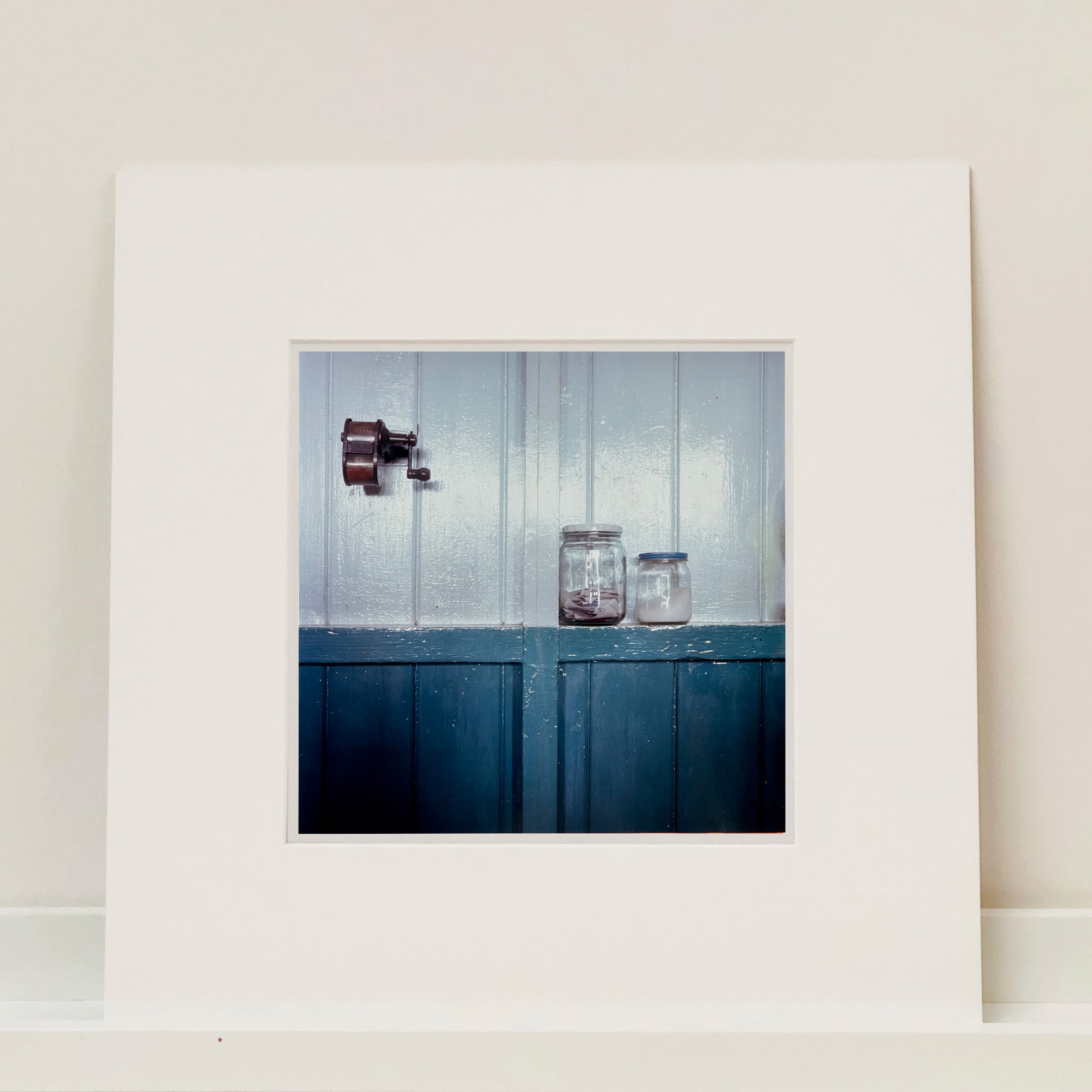 Photograph by Richard Heeps. A pencil sharpener is attached to the white part of a two-tone wall.  Halfway down the wall turns blue and here is a shelf providing a narrow home to two screw-top jars. 