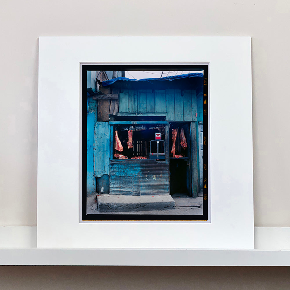 Photograph by Richard Heeps. A butcher's window in the North of India.  A blue painted shack with meat hanging in the window and door.