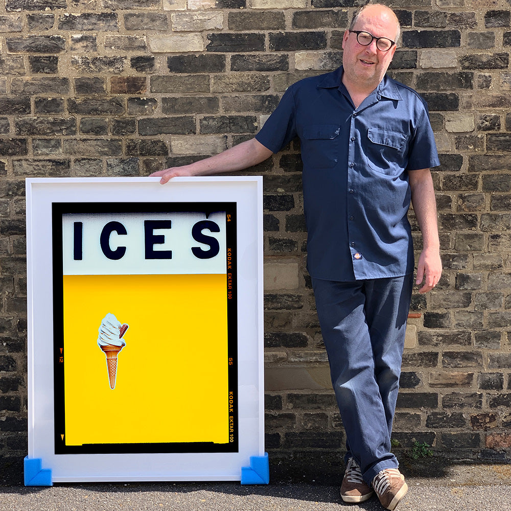 White framed photograph held by photographer Richard Heeps. Richard holding a large framed print of an ice cream on a colour block (yellow) with ICES written across the top of each and each has a Kodak film rebate.