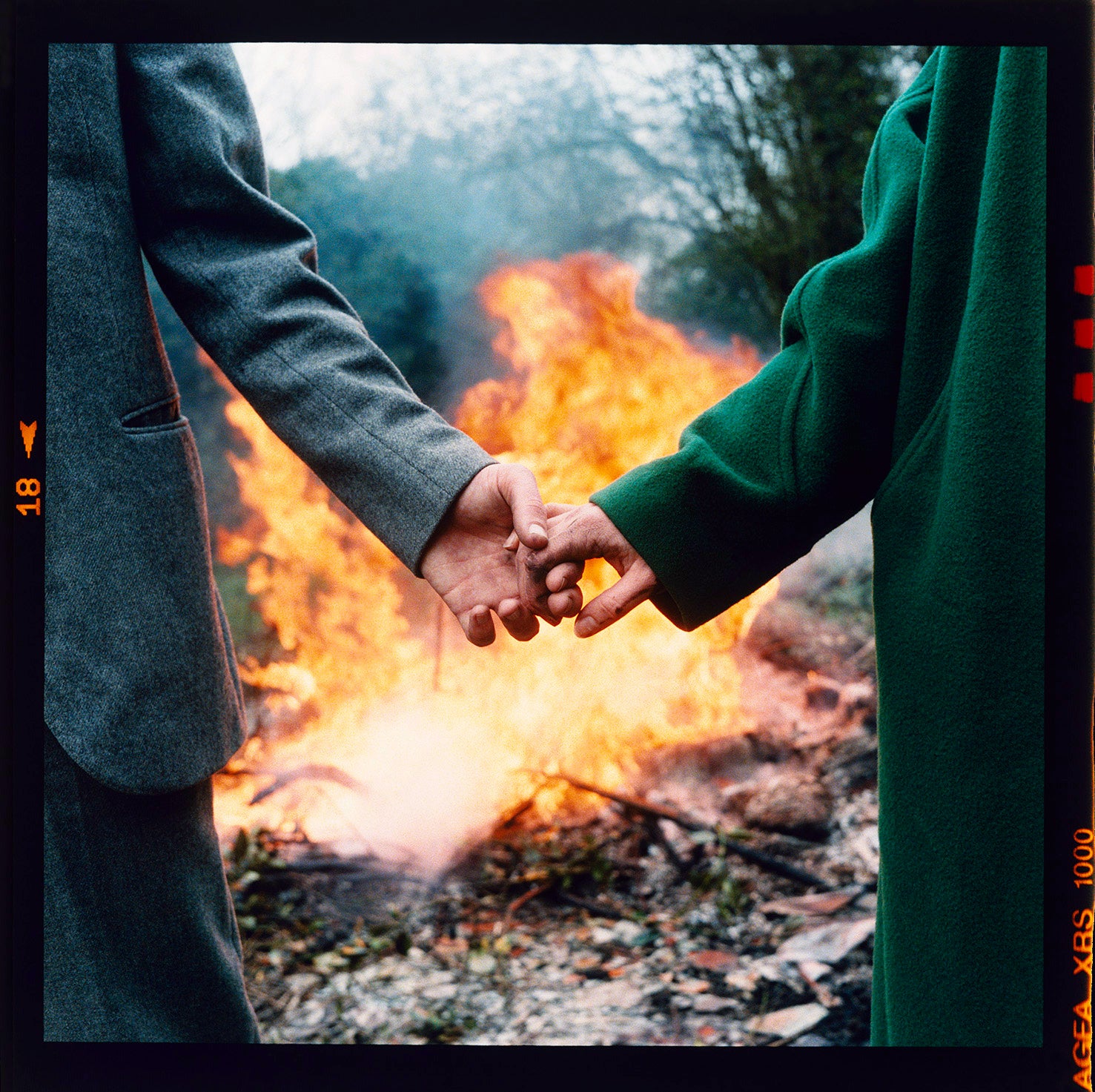 Two people in in winter coats hold hand by a fire outdoors at Wysing Arts Centre Cambridge.