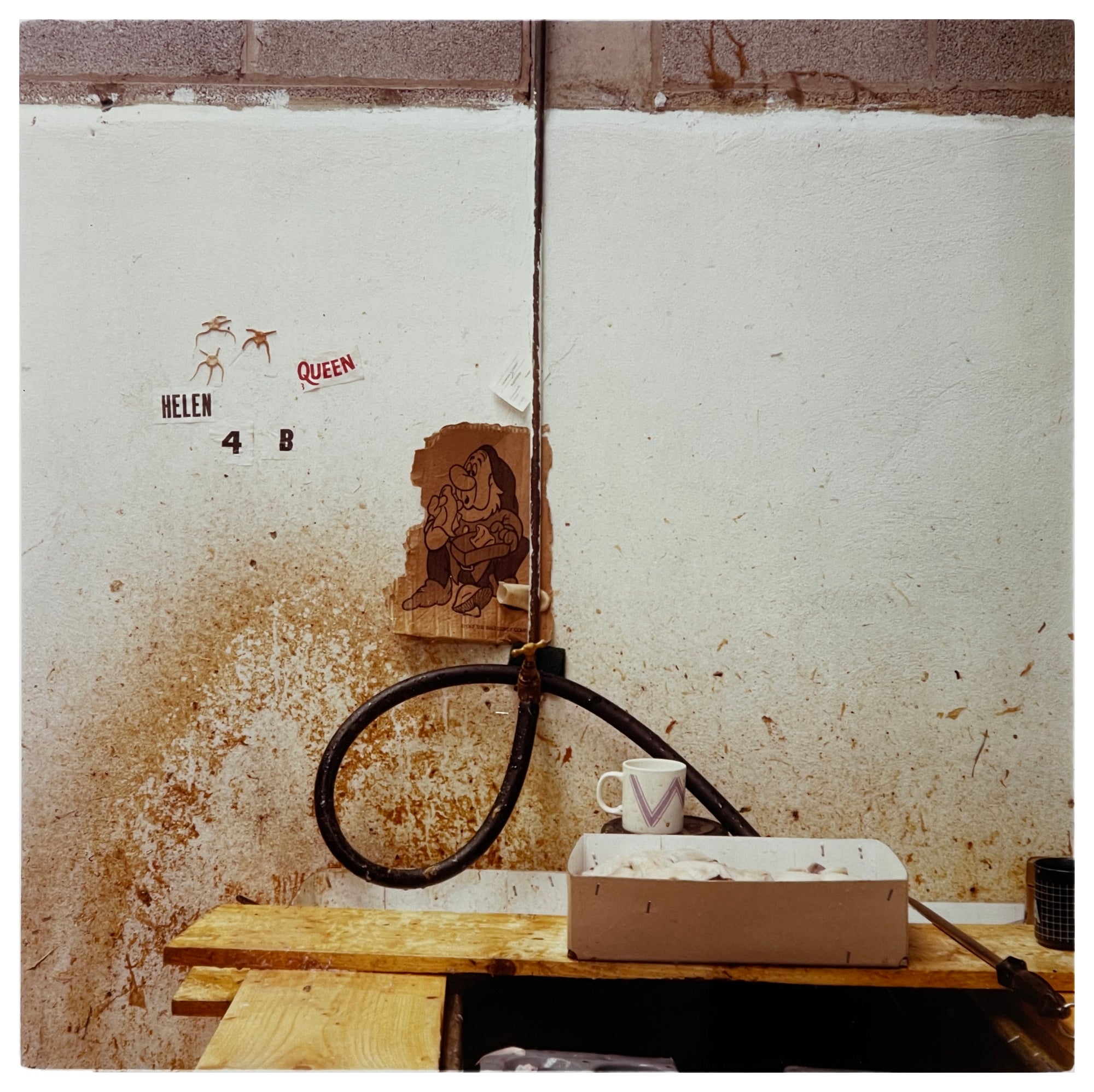 Photograph by Richard Heeps.  A bare wire is knotted on a dirty cream wall.  Stuck behind the main vertical wire is a picture of the Disney character Sneezy on a torn off bit of card.