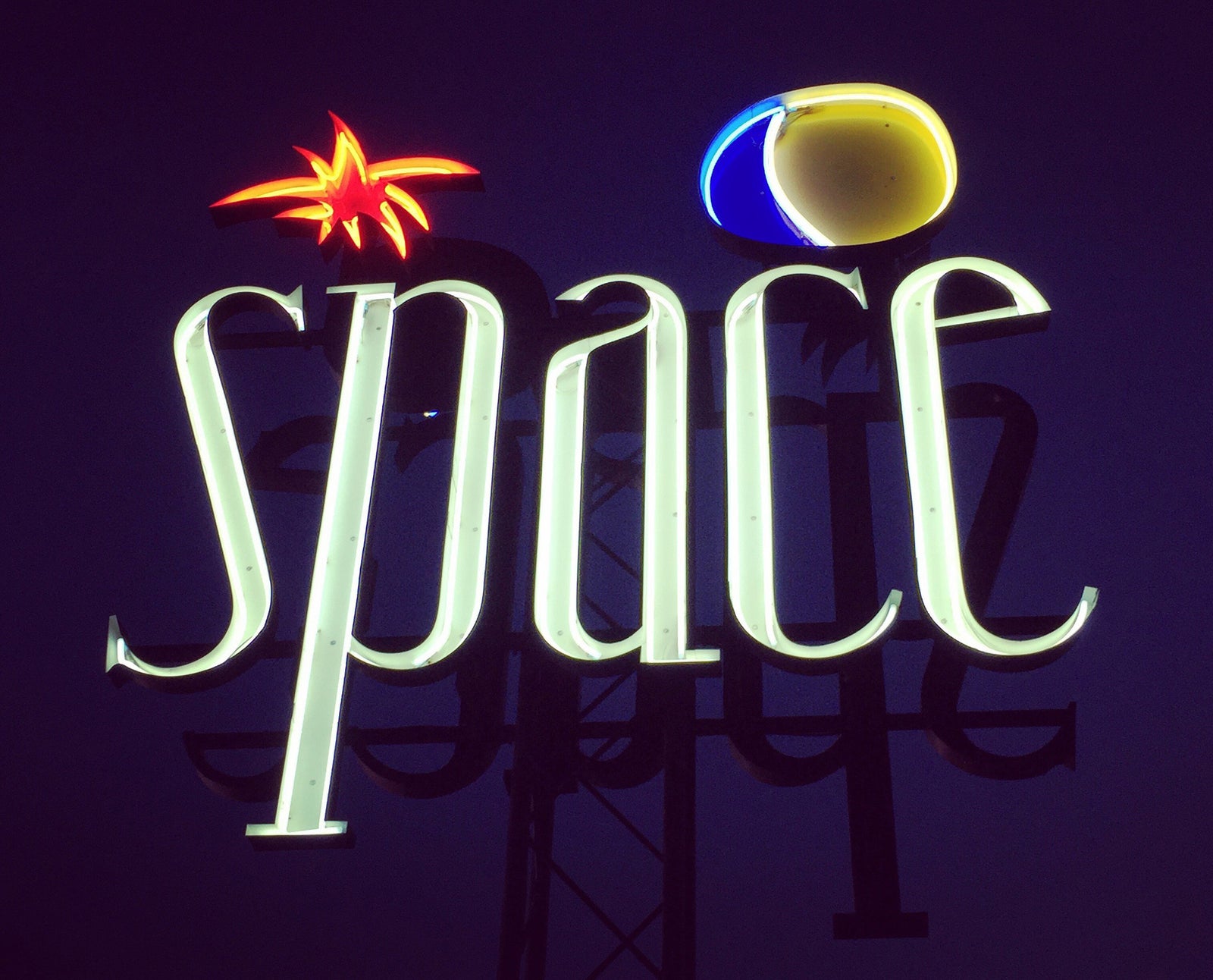 'Space', features neon lettering against an inky blue sky. The subject is a roadside sign taken in Ibiza during the final year of the iconic super club 'Space'. 