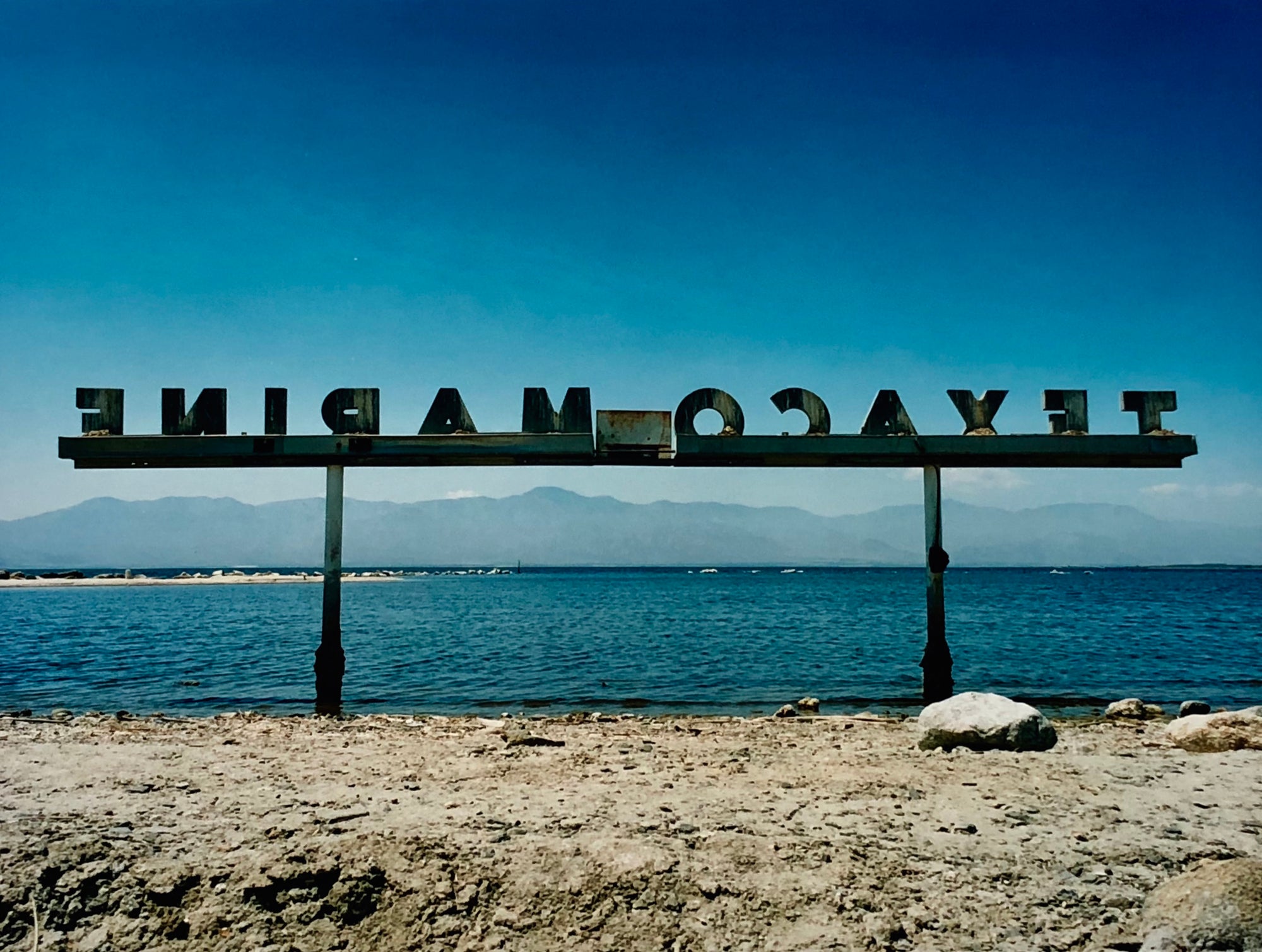 Texaco Marine sign on the Salton Sea beach, with a blue sky and mountains in the distance