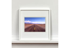 'The Road to Death Valley', taken in the Majova Desert, California, features a clouded blue sky met my mountains on the horizon. This American landscape artwork is part of Richard Heeps' 'Dream in Colour' series.