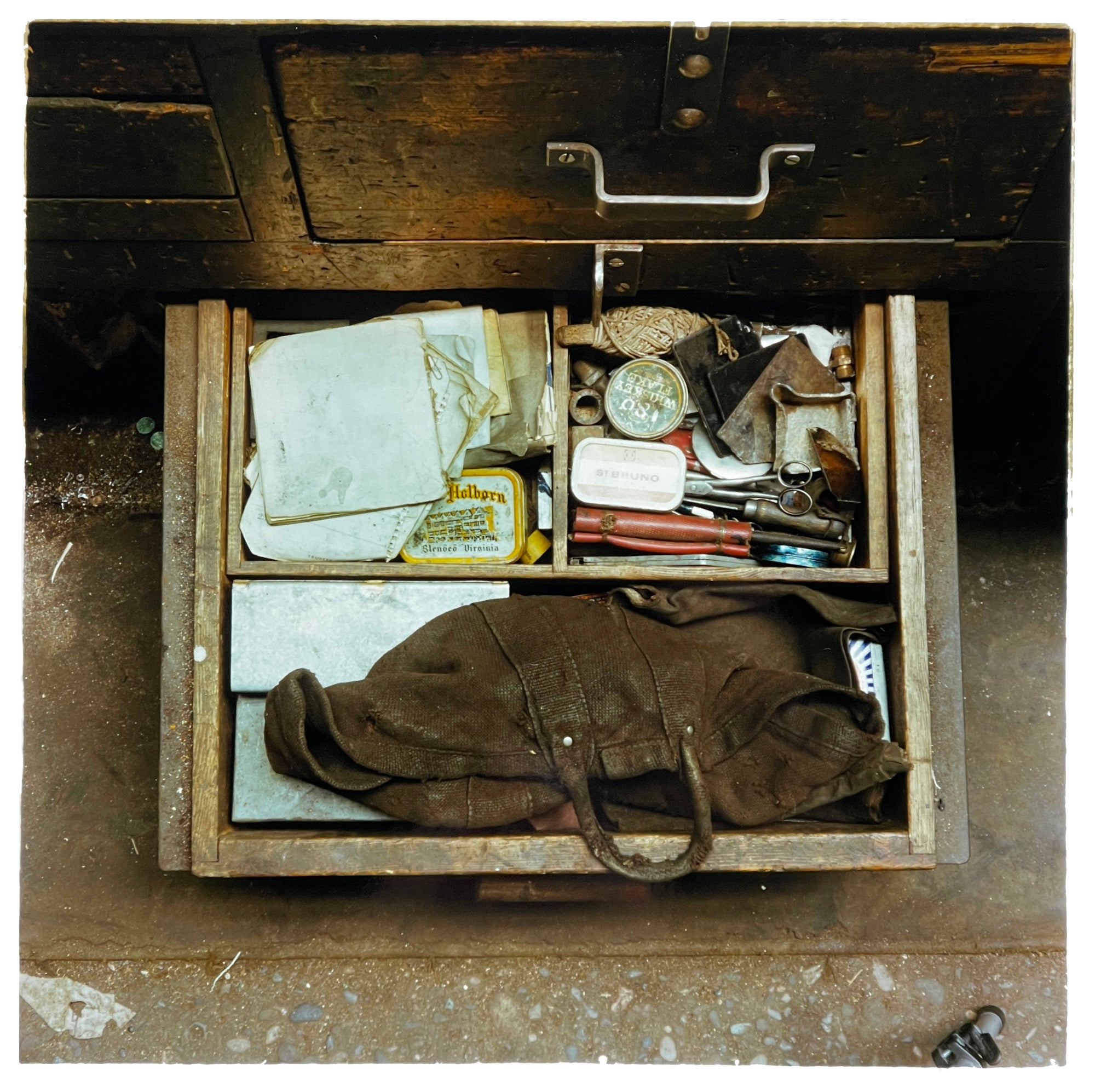 Photograph by Richard Heeps.  The bottom drawer of a battered wooden work desk is open.  There is tobacco, a worn leather tool bag, a spool of string, scissors and other paraphernalia.