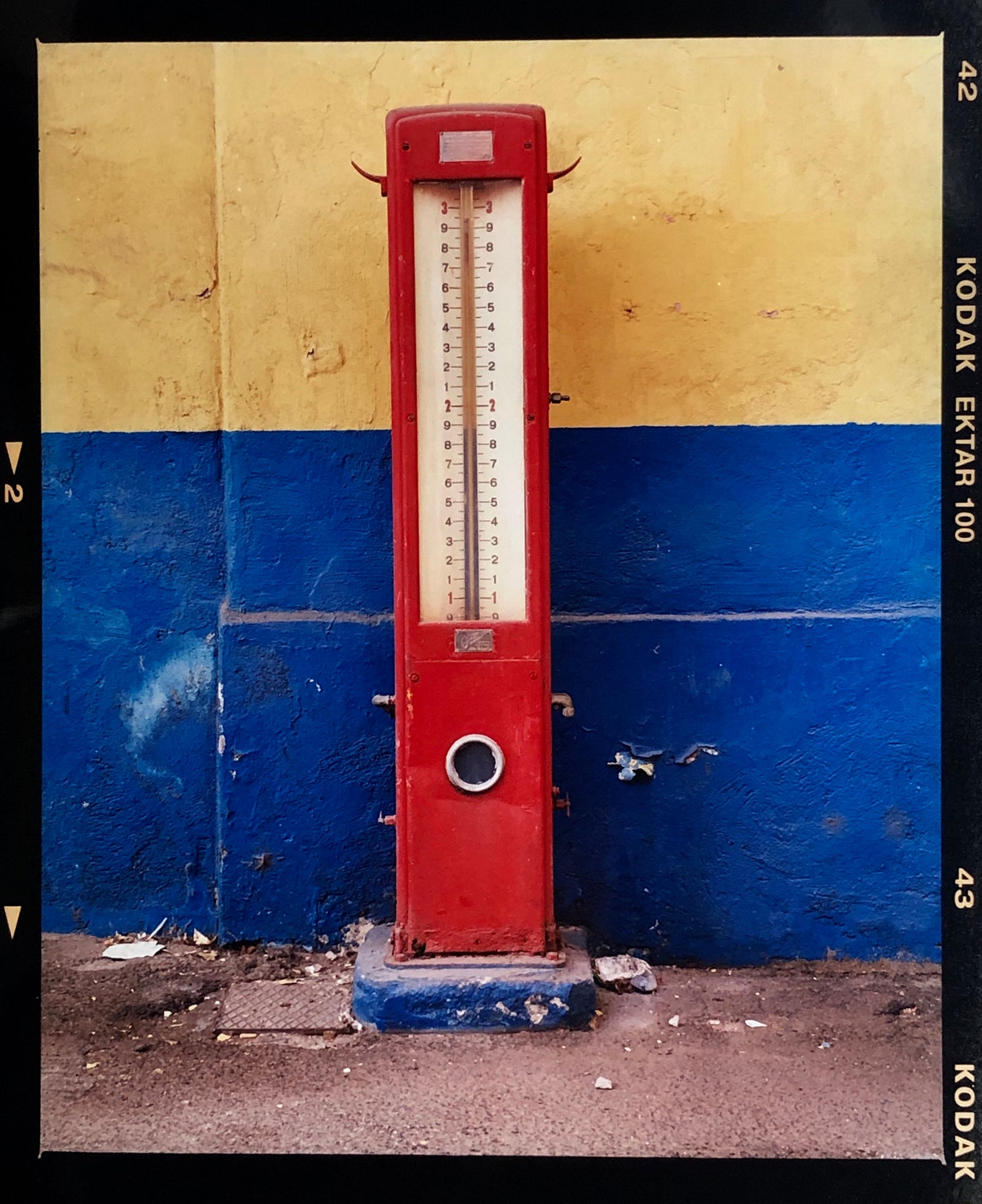 A red retro tyre pump against a yellow and blue painted wall, in the Porta Genova area of Milan.