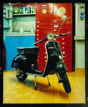 A black vespa against a red, blue and yellow interior. Photographed in Milan, Italy. 