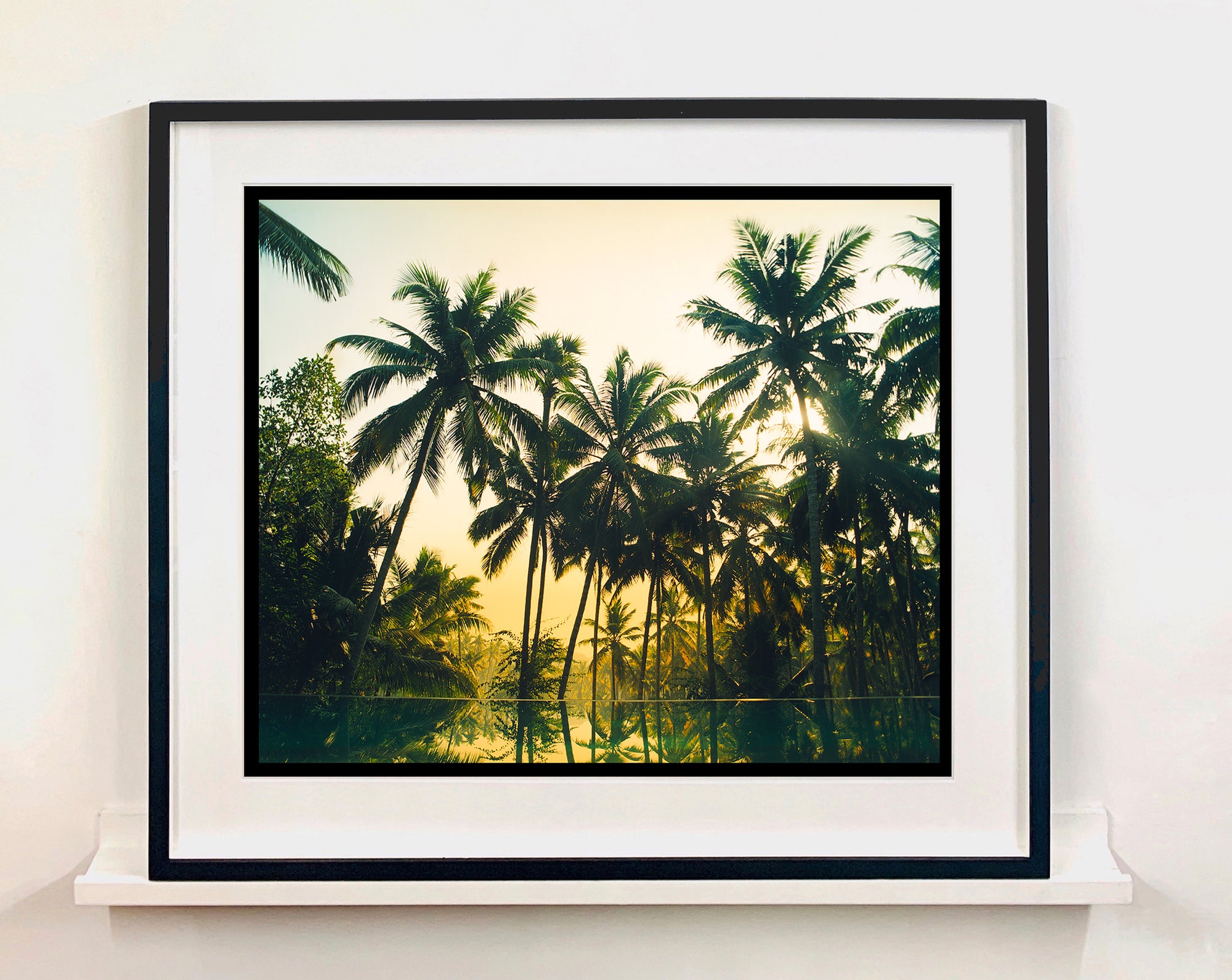 Palm trees stand strong against a setting sun, reflecting gracefully in the water below in this artowork 'Vetyver Pool', taken in Poovar, Kerala in 2013. This gorgeous palm tree print has warming tones and will take you somewhere tropical. Richard Heeps is inspired by films, often referencing them in day to day life and on this journey he had 'Apocalypse Now' on his mind.